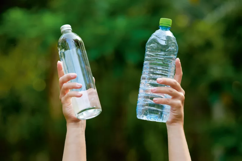 Zwei Hände halten eine Einwegflasche und eine Mehrwegflasche